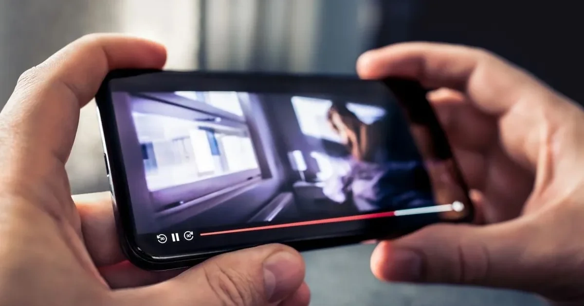 Hands holding a phone playing a movie with the playback timeline visible while multitasking with a floating video window